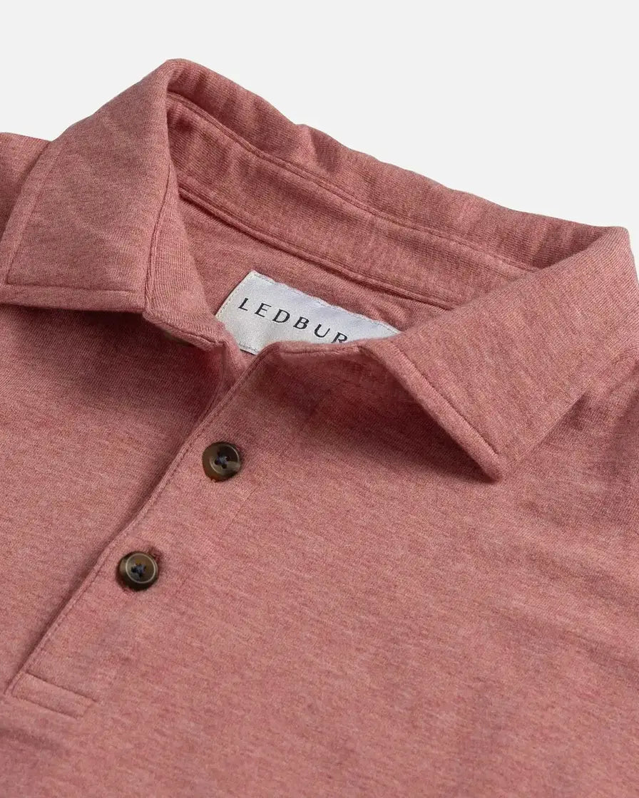 Close-up of a heathered light red polo shirt with a white Ledbury neck label and two dark buttons, photographed on a light gray background.
