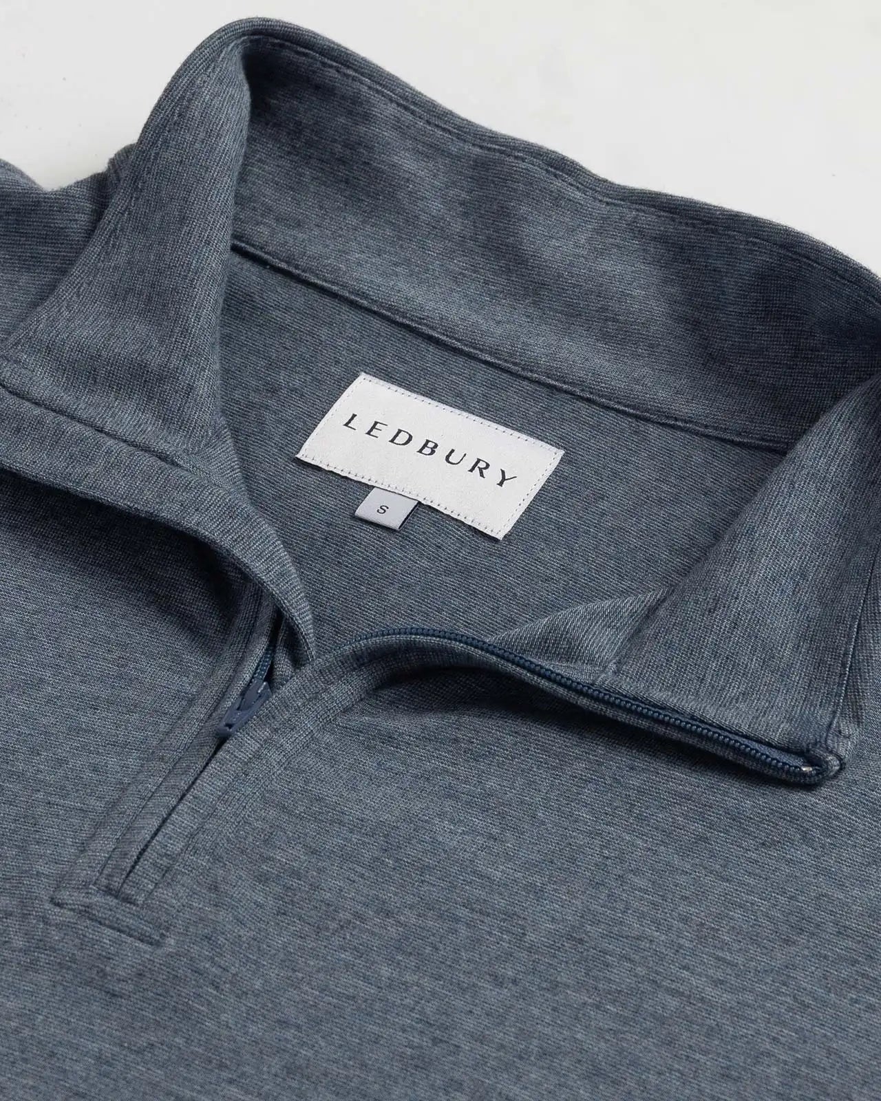 Close-up of a heather blue quarter-zip pullover sweater with a collar, showing the LEDBURY brand label inside the neck.