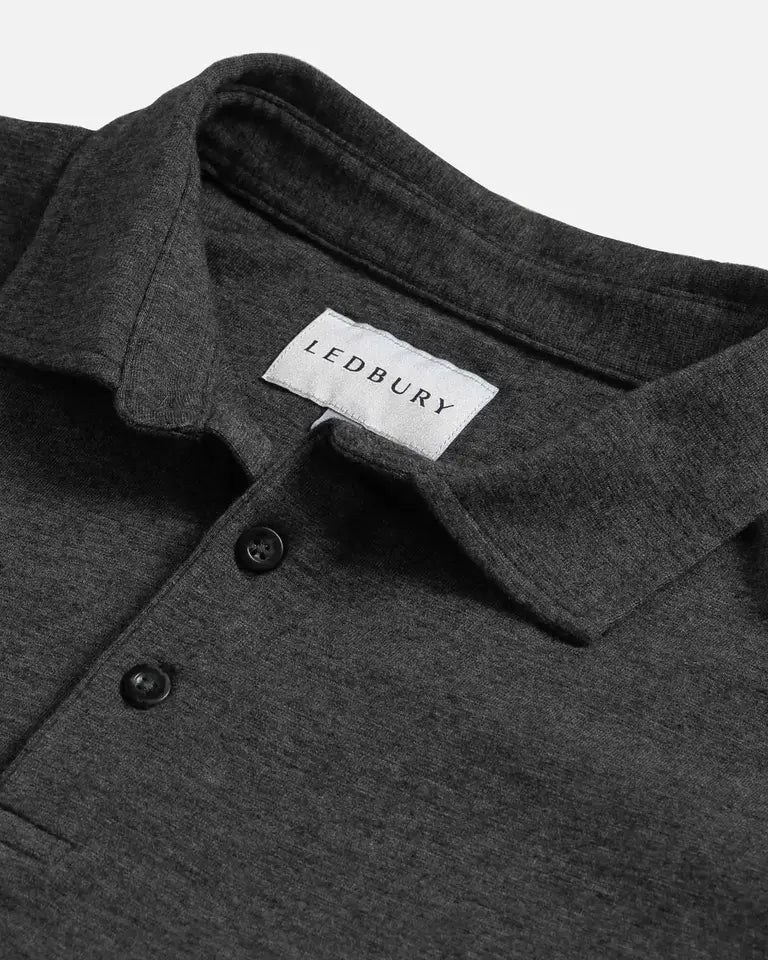 Close-up of a dark heather gray polo shirt collar with a white LEDBURY neck label and two dark buttons, photographed on a light gray background.