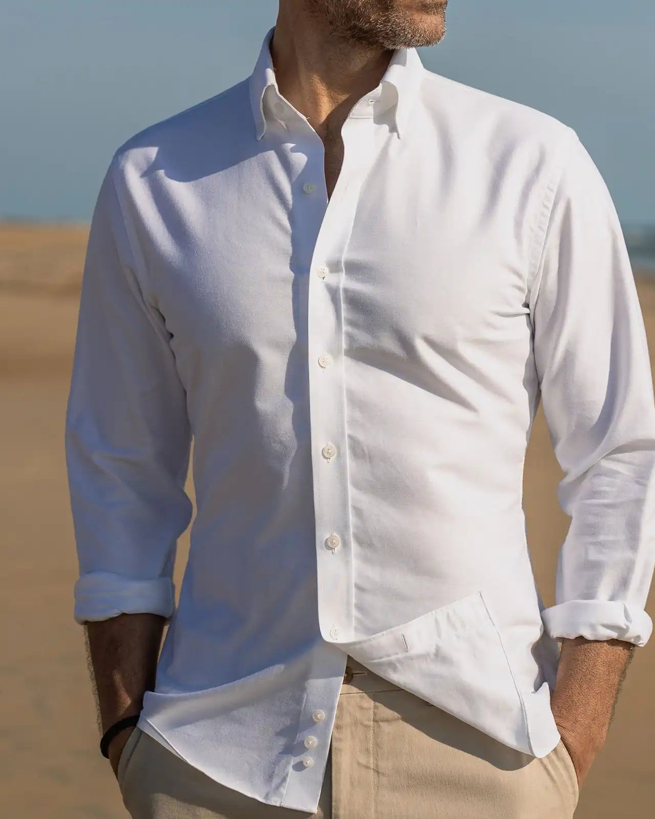Man wearing a the white Mayfield Oxford button-up shirt with rolled-up sleeves on a beach.