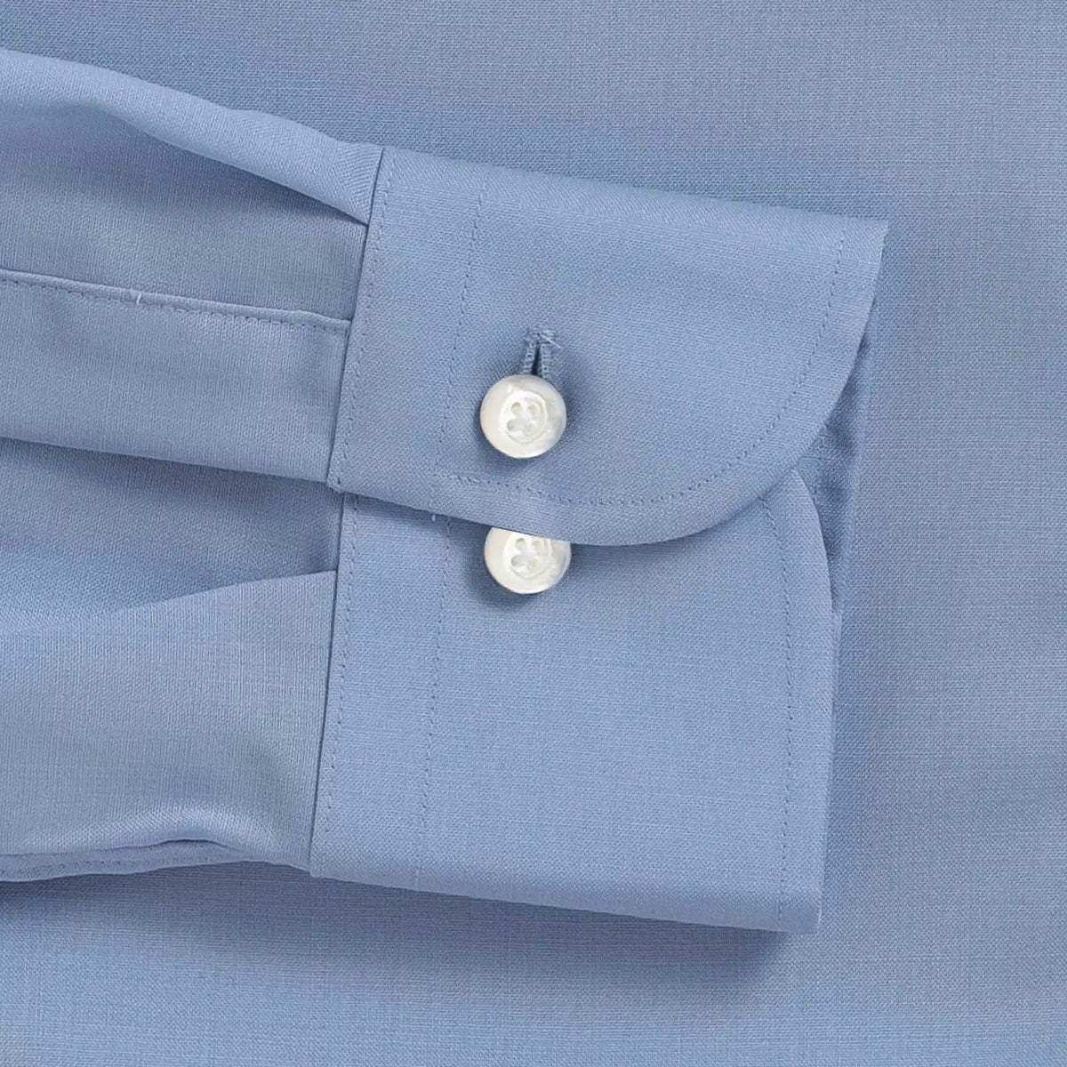 Close-up of a light blue dress shirt cuff with two white mother of pearl buttons on a matching blue fabric background.