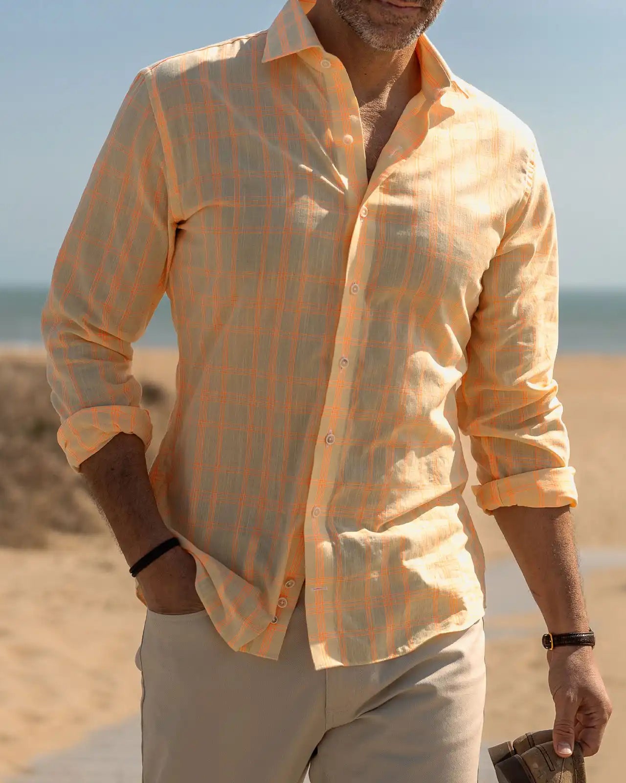 Man wearing a bright yellow and orange checkered shirt on a beach
