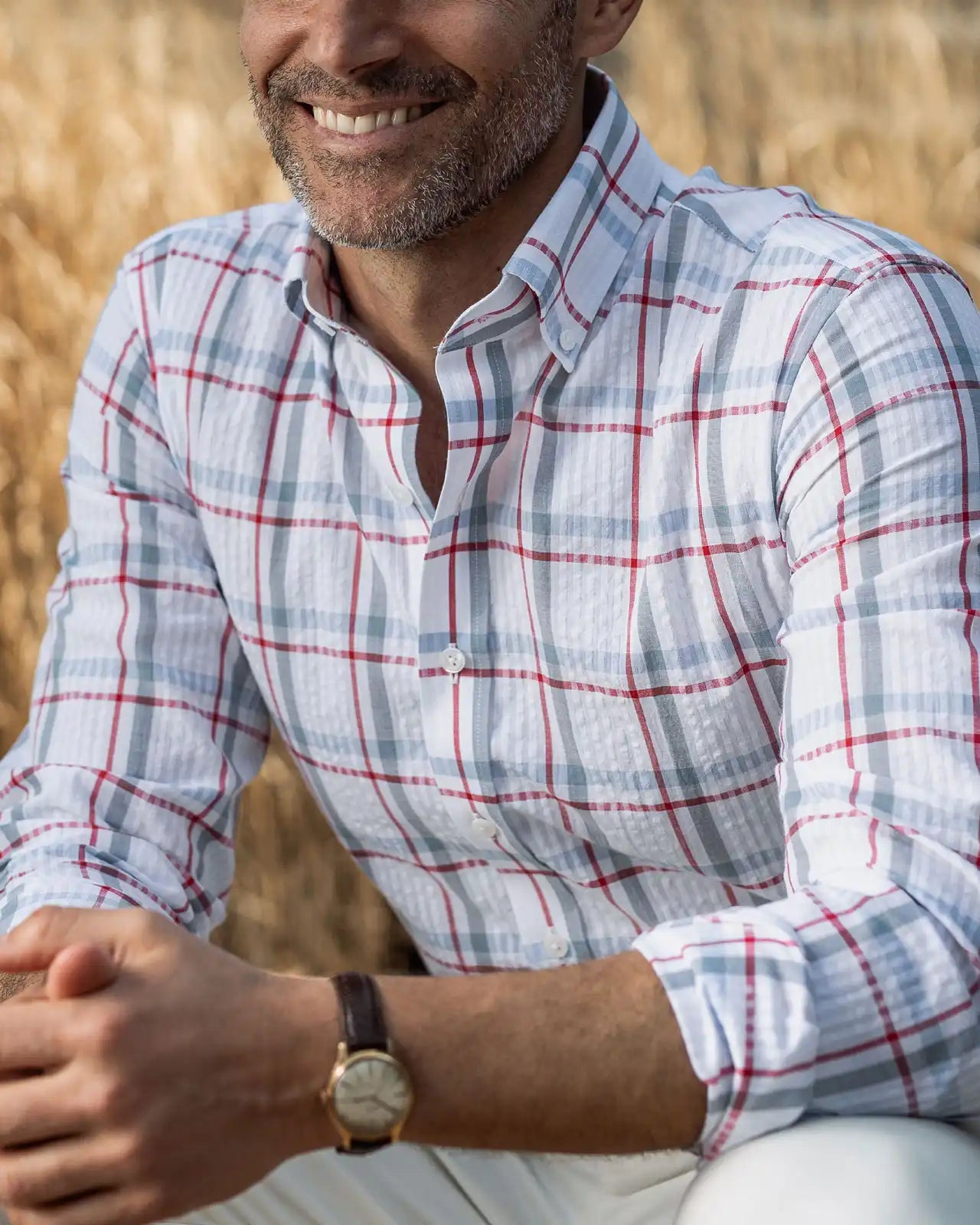 Man wearing the Ledbury Red Pepper Bartlett Plaid shirt in a field — pepper red, white, and blue cotton seersucker