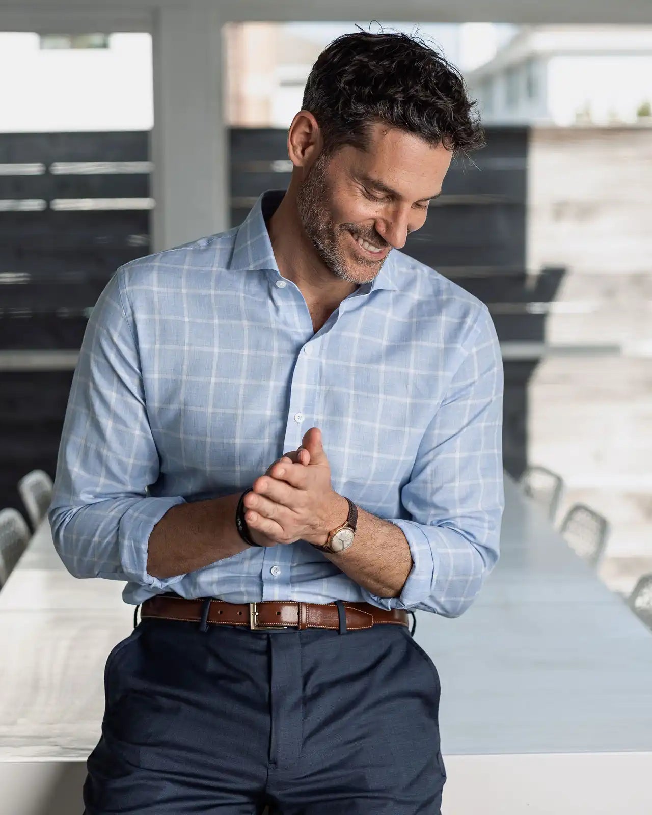 Man wearing a light blue checkered shirt and dark pants in a modern room.