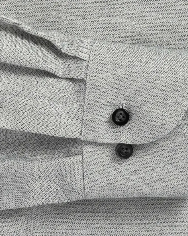 Close up of the sleeve of a grey small scale herringbone dress shirt with black buttons