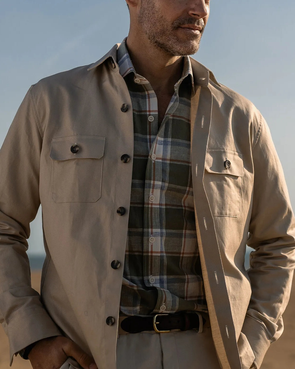 Man wearing a light tan shirt jacket over a plaid shirt with a blurred background