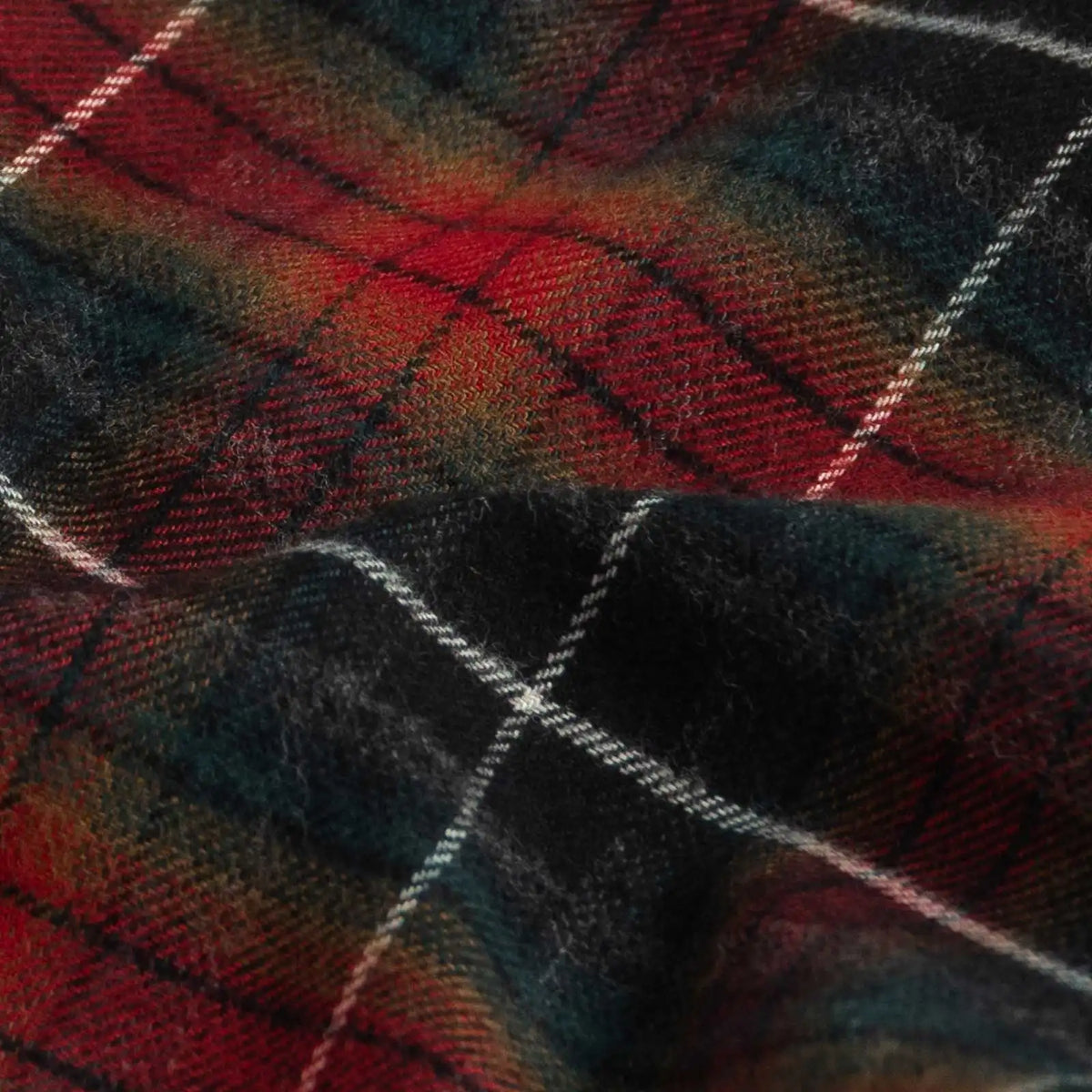 A close-up of a plaid fabric with a tartan pattern in red, black, and green, accented by thin white diagonal stripes.