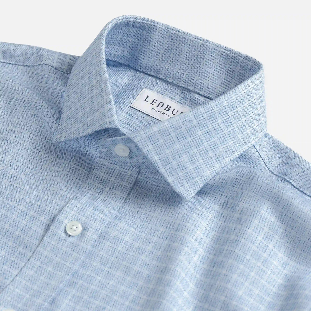 Close-up of a light blue and white checkered button-down shirt collar with a visible LEDBUDD brand label.