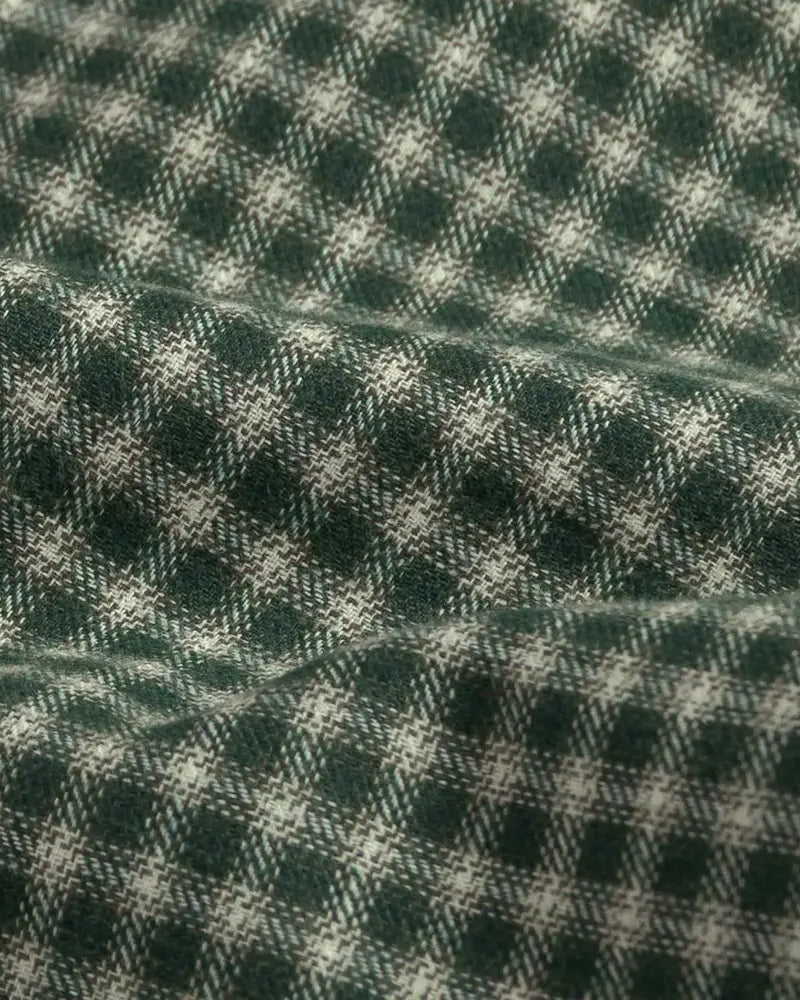A close-up of a dark green and off-white plaid fabric with a soft, draped texture.