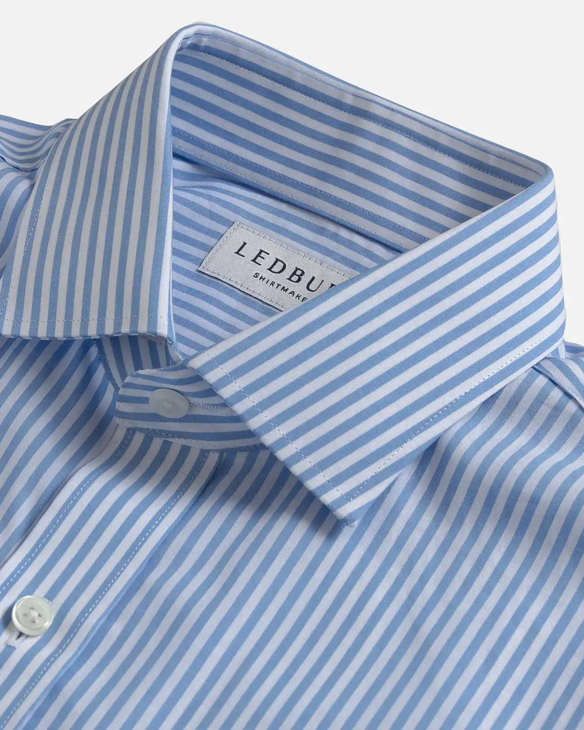 A close-up of a light blue and white striped dress shirt by Ledbury, showing the collar, button placket, and woven brand label.