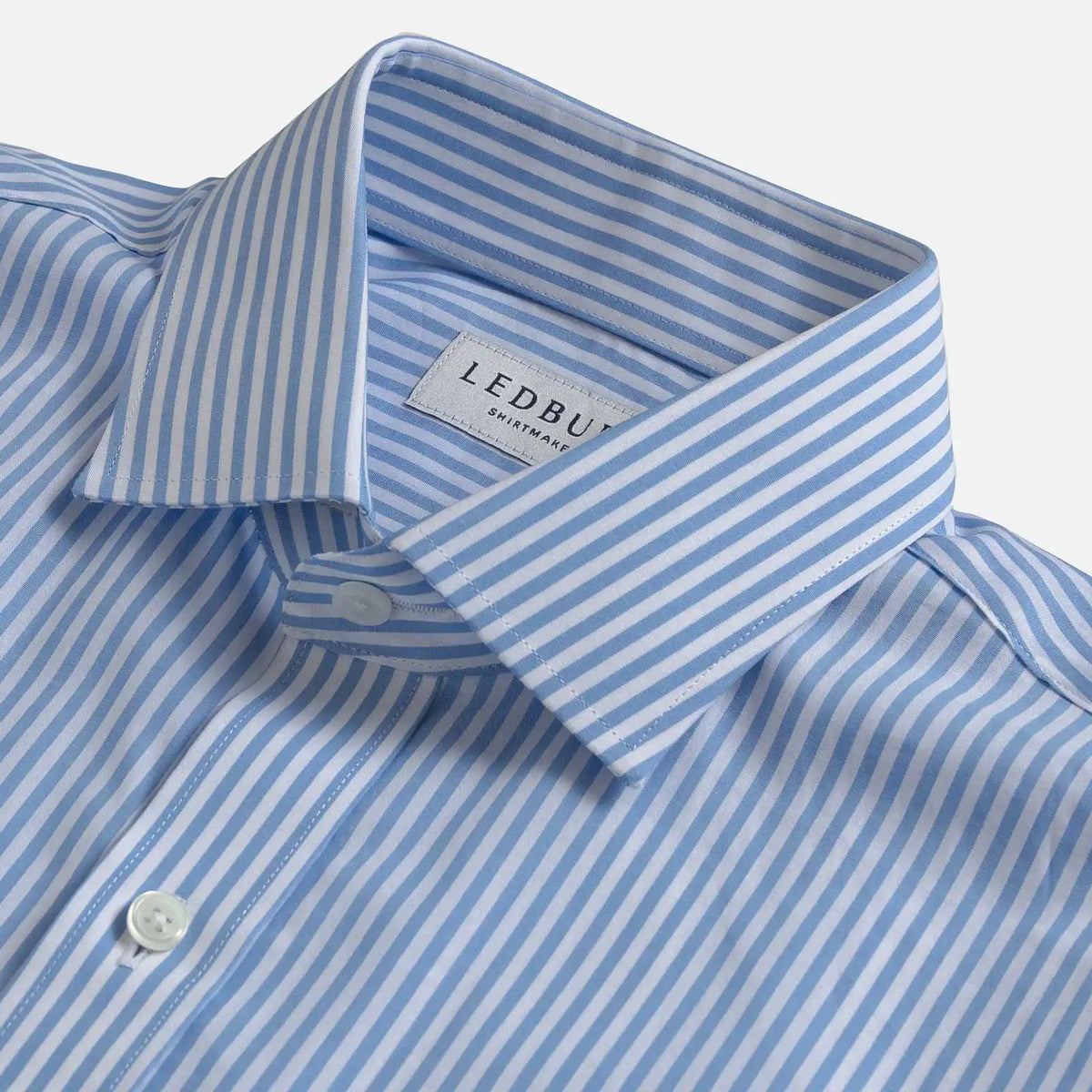 A close-up of a light blue and white striped dress shirt by Ledbury, showing the collar, button placket, and woven brand label.