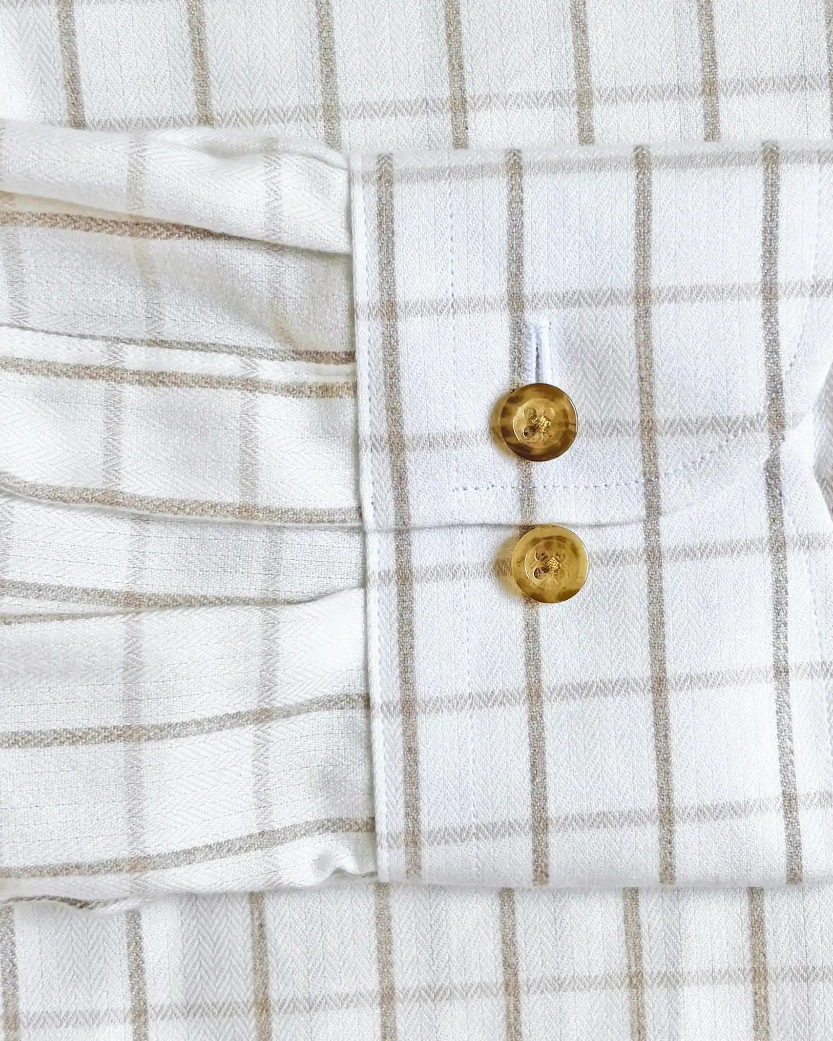 Close-up of a white and beige windowpane plaid shirt showing the buttoned cuff with gold-toned buttons.