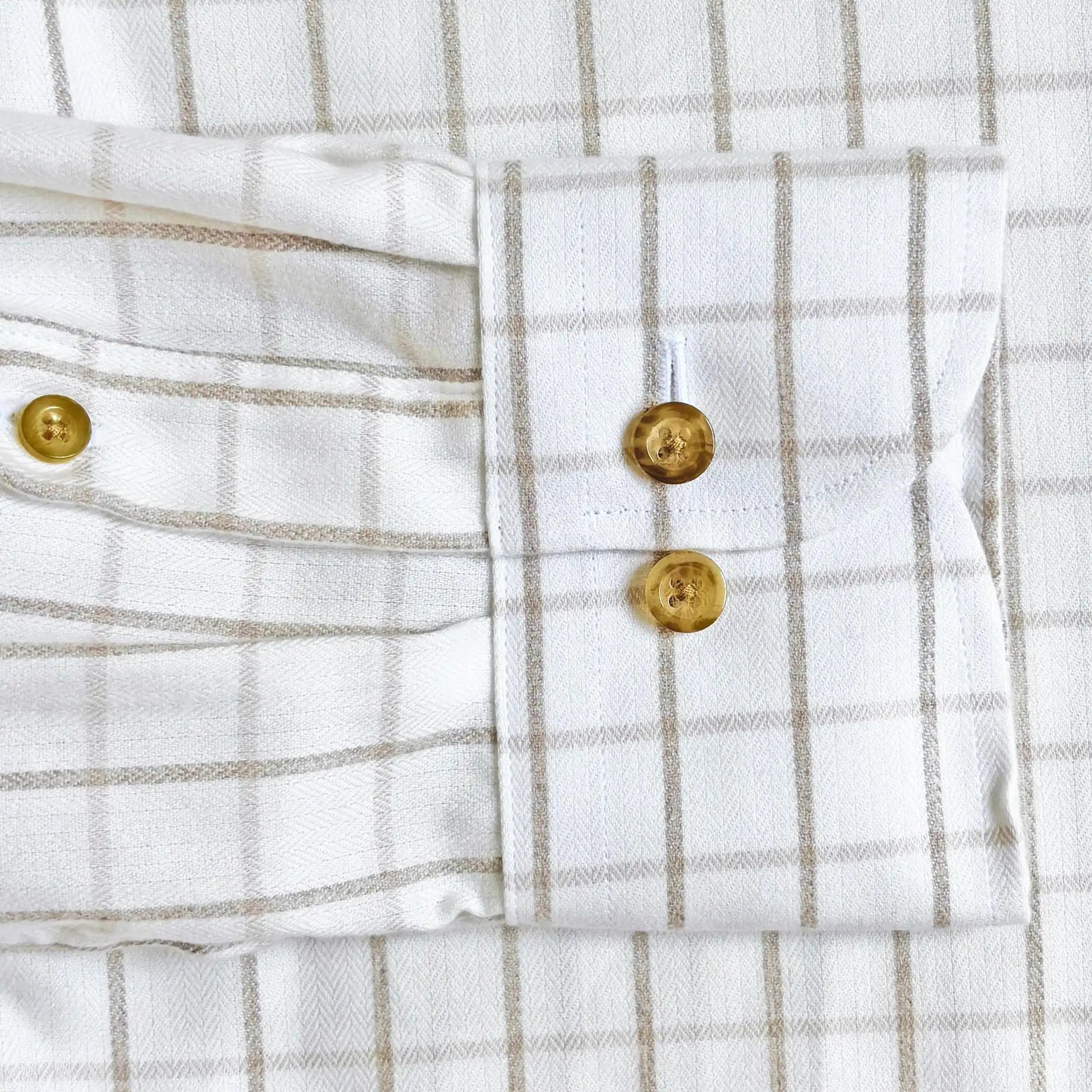 Close-up of a white and beige windowpane plaid shirt showing the buttoned cuff with gold-toned buttons.