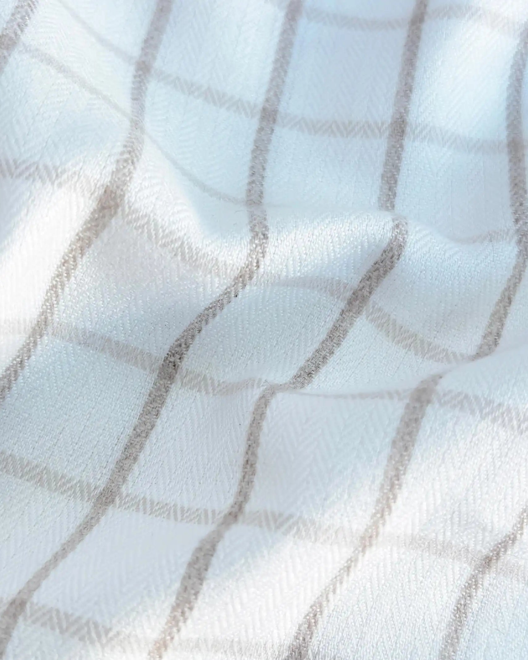 A close-up of a white fabric with a soft gray plaid pattern, showing the texture and folds of the material.