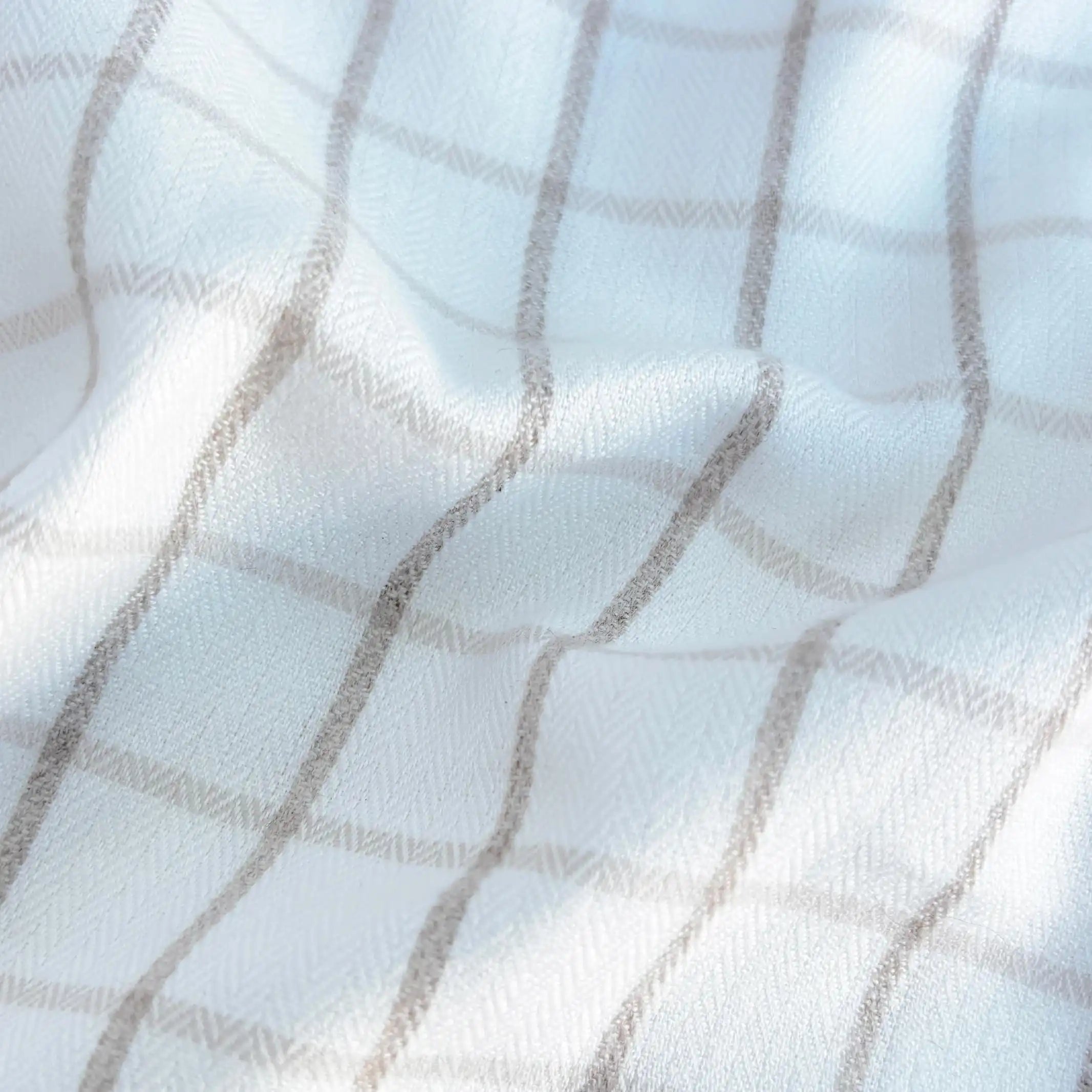 A close-up of a white fabric with a soft gray plaid pattern, showing the texture and folds of the material.