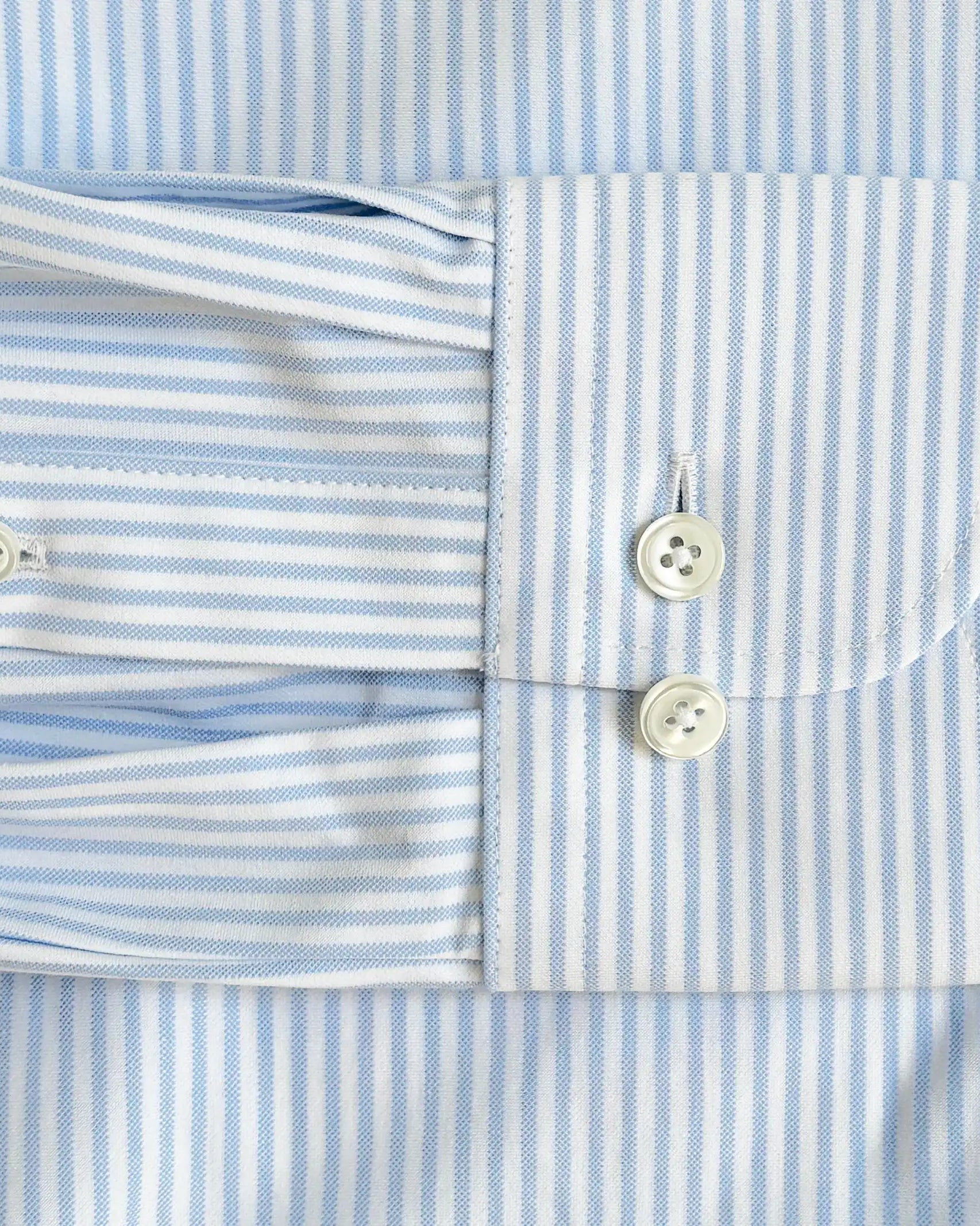 Close-up of a light blue and white striped dress shirt cuff with two white buttons, showing the fabric texture and pattern details.
