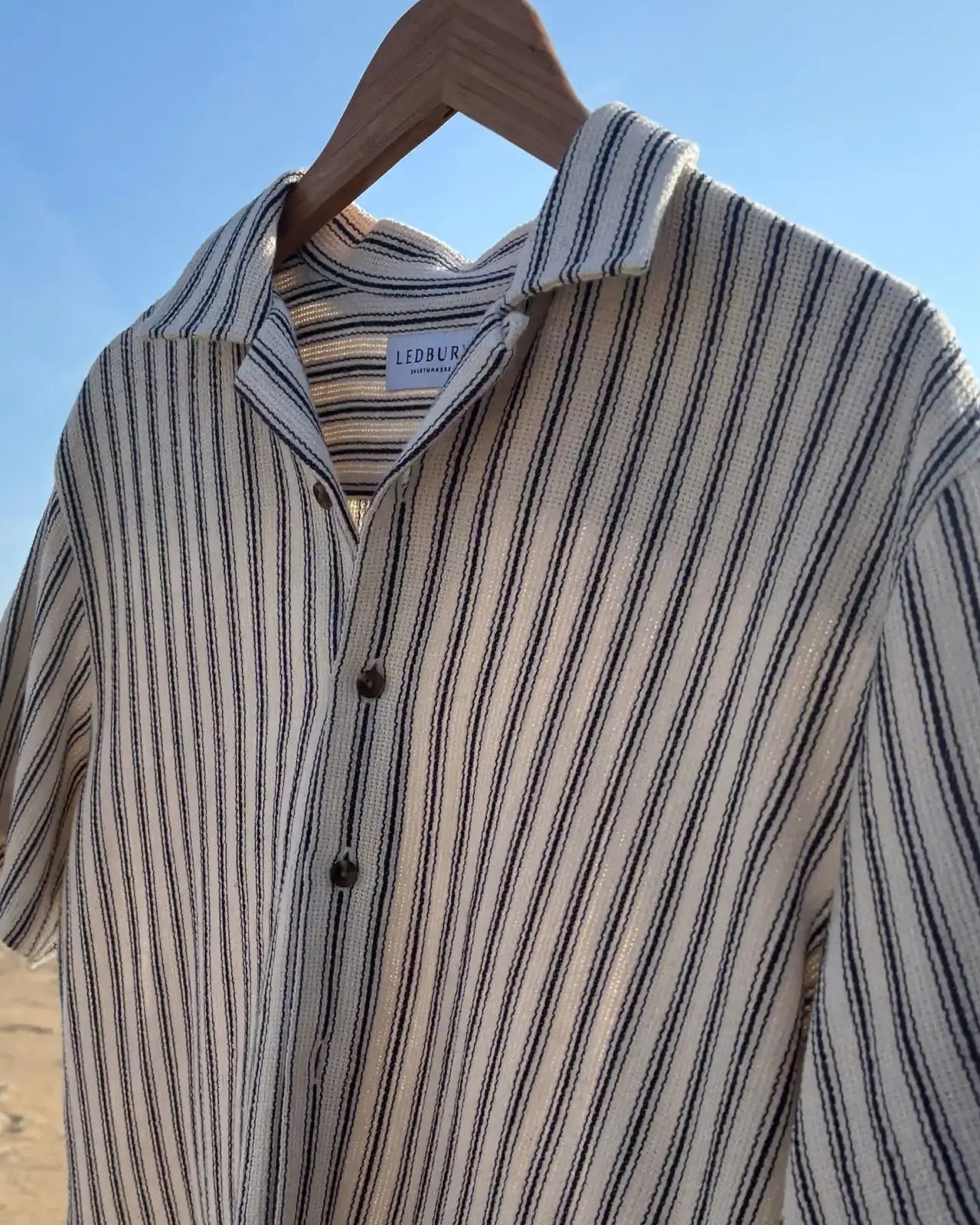 Ledbury navy and cream striped camp collar shirt hanging on a hanger at the beach
