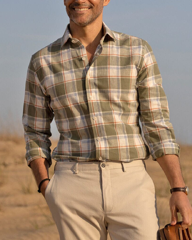 Man wearing a plaid shirt and beige pants standing on the beach