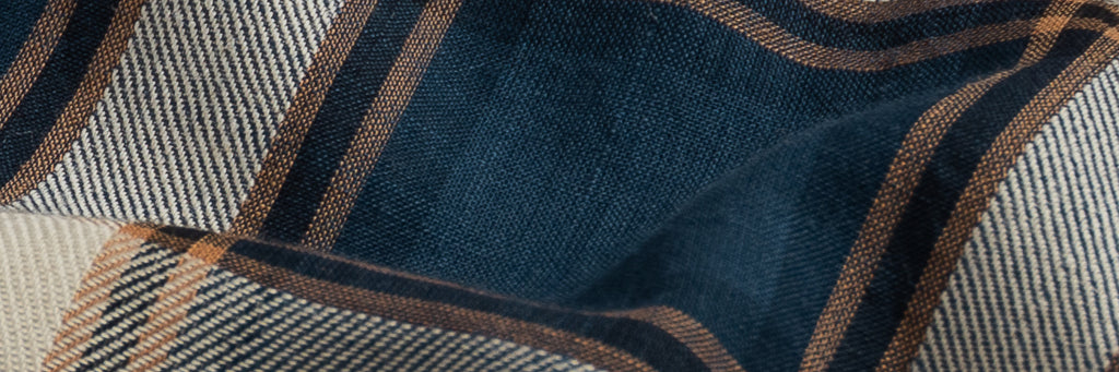 Closeup of the fabric of a men's Italian woven navy, burnt orange and tan summer weight plaid button down shirt