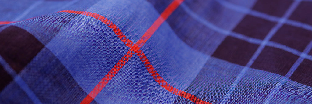 Closeup of the fabric of a men's royal blue, black and red bold summer weight plaid button down shirt 
