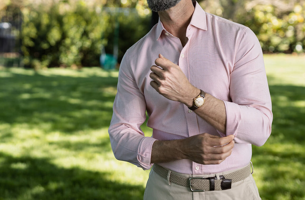 Image of a model standing in a grassy field wearing a solid colored button down shirt
