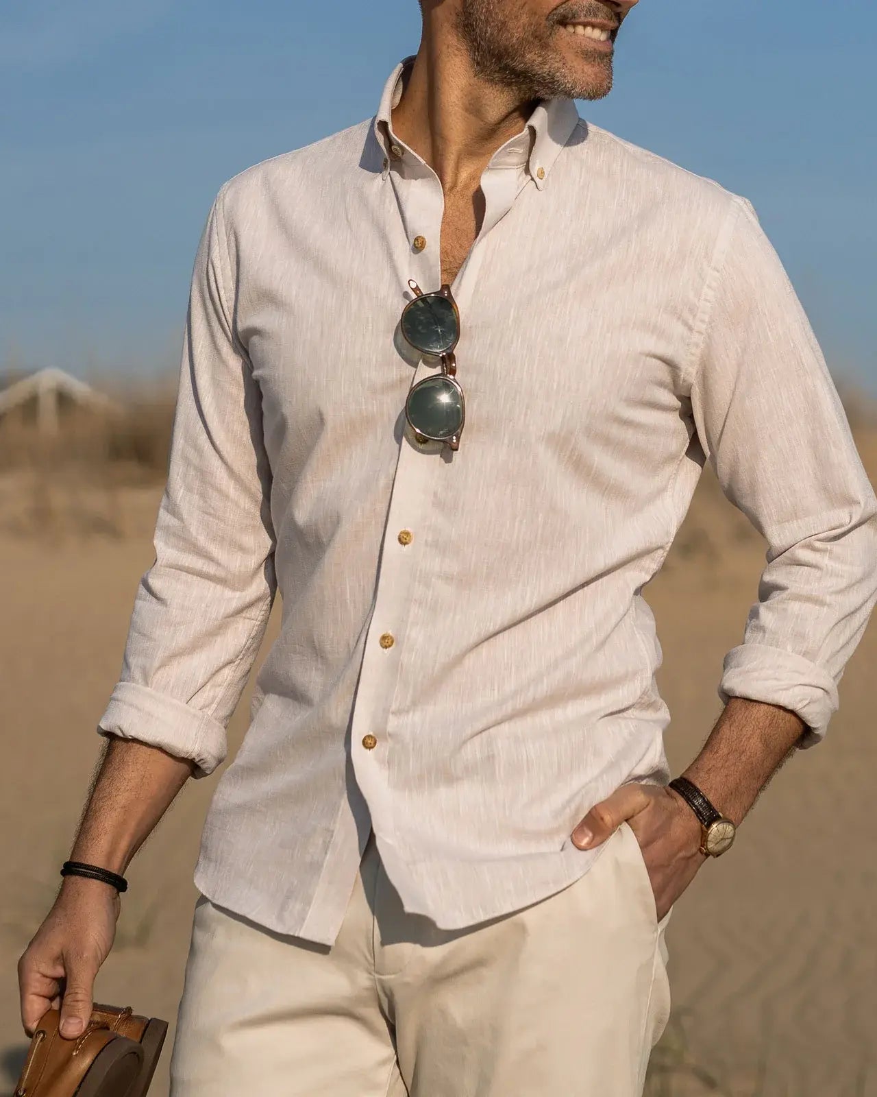 Man wearing a light-colored Ledbury button down shirt with rolled-up sleeves in a beach setting