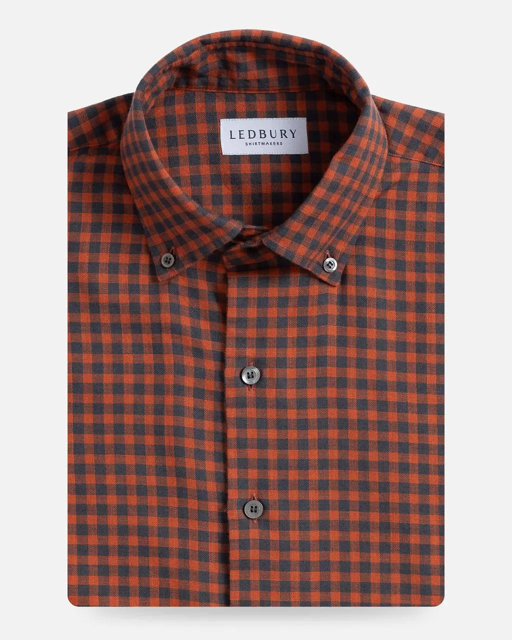 A folded men's button-down shirt by Ledbury, featuring a burnt orange and dark grey gingham check pattern, displayed on a clean light gray background.