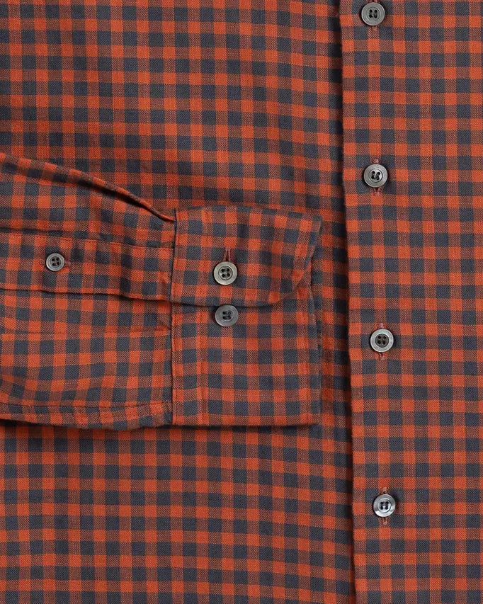 Close-up of a burnt orange and dark gray checkered plaid button-down shirt, showing a chest pocket with buttoned flaps and gray buttons.