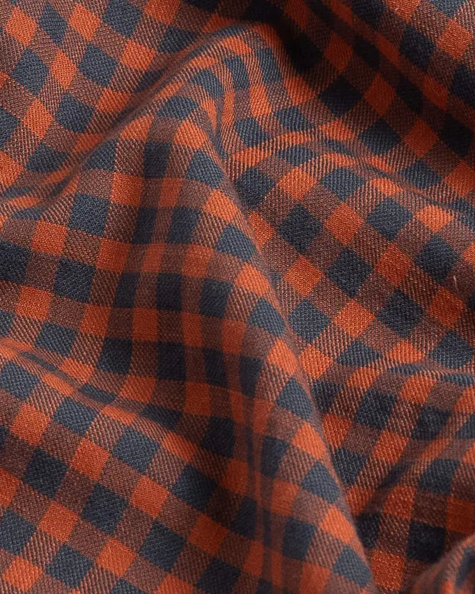 A close-up of draped fabric with a classic gingham pattern in rust orange and dark grey.