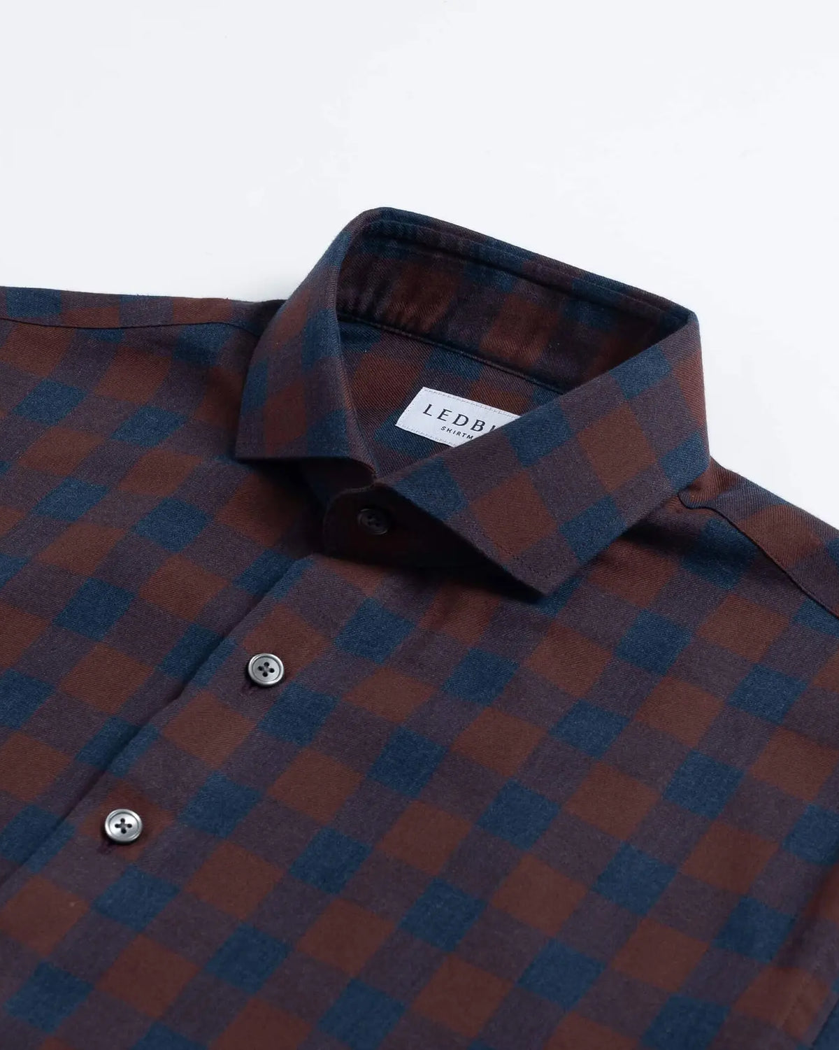 A close-up of a Ledbury brand long-sleeve button-down shirt featuring a dark red and navy blue checkered pattern, with a white neck label.