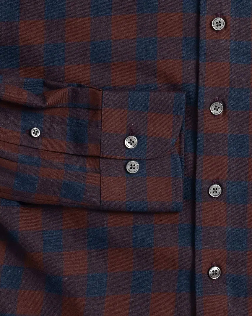 Close-up of a plaid button-up shirt in dark red and navy blue, showing a chest pocket with a flap and smoke grey buttons.