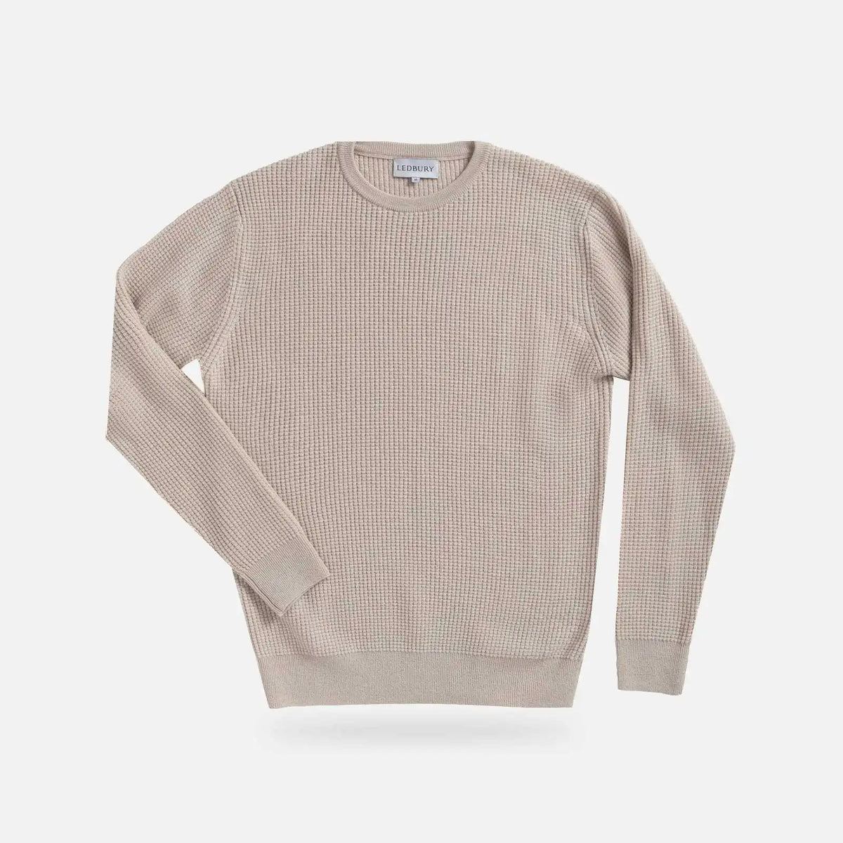 A light beige ribbed knit crewneck sweater with long sleeves, displayed flat against a light gray background.