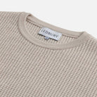 Close-up of a ribbed knit crewneck sweater in a light beige color, showing the interior neck label with the brand name LEDBURY.