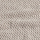 Close-up of a waffle-knit fabric in a light oatmeal beige color, showing the textured grid pattern and soft folds.