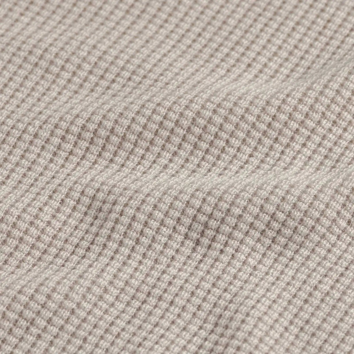 Close-up of a waffle-knit fabric in a light oatmeal beige color, showing the textured grid pattern and soft folds.