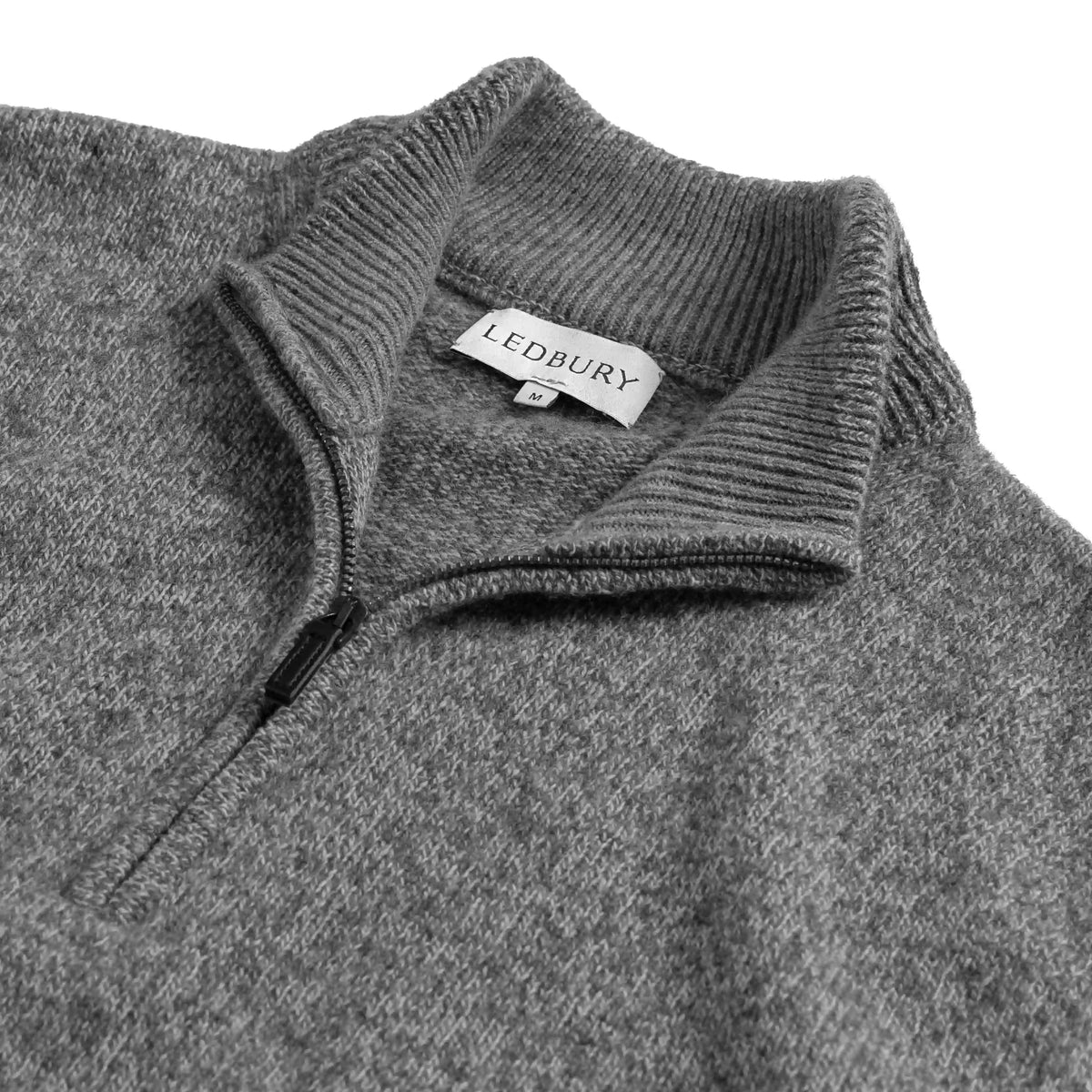 Close-up of a gray ribbed knit quarter-zip sweater with a white LEDBURY neck label, shown against a white background.
