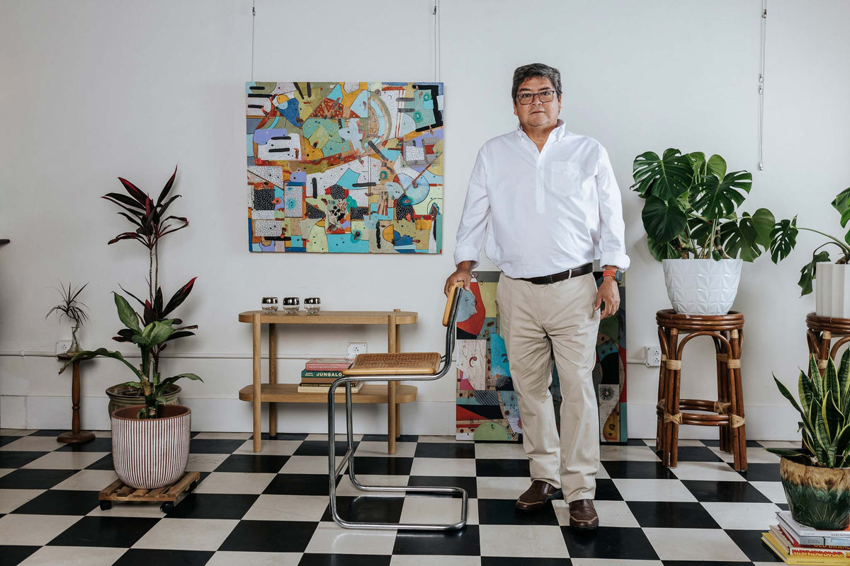Man standing in a room with checkered floor, plants, and colorful wall art.