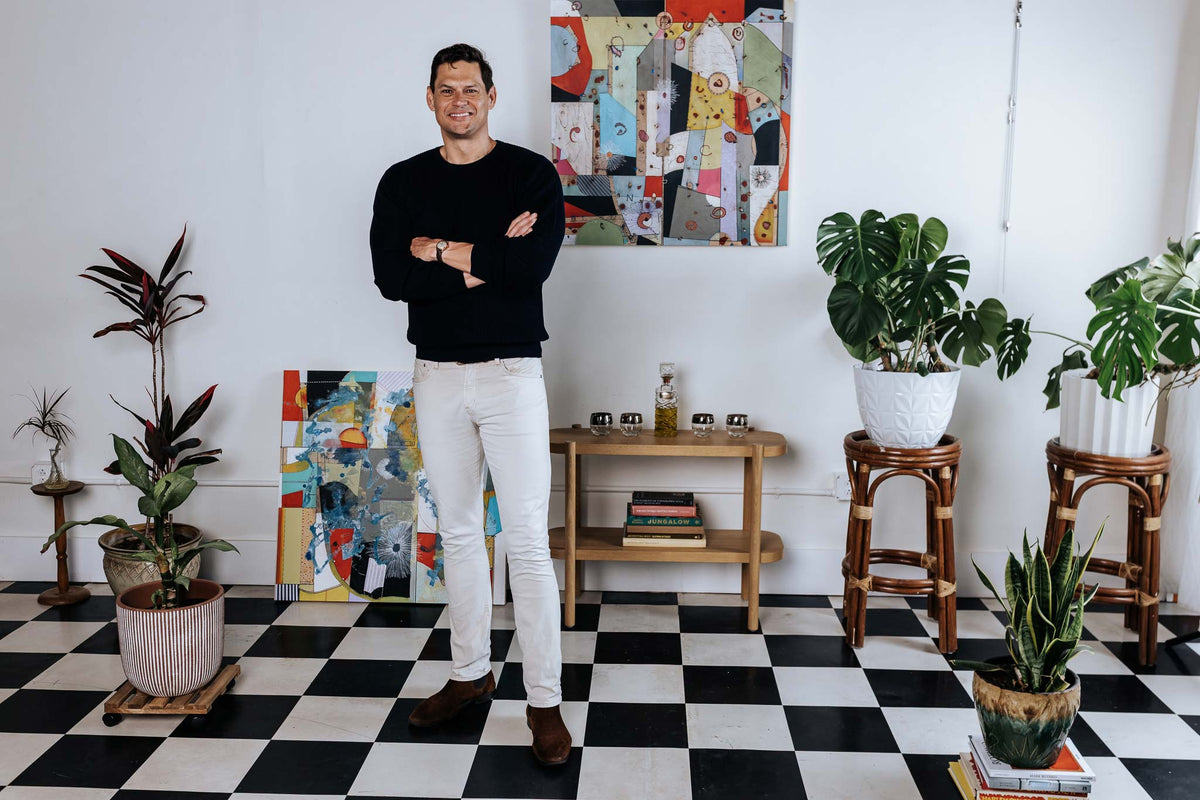 Man standing in a room with checkered floor, plants, and colorful artwork.