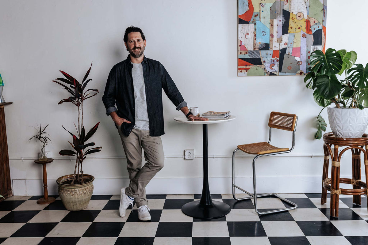 Man standing in a stylish room with a checkered floor, plants, and a table.