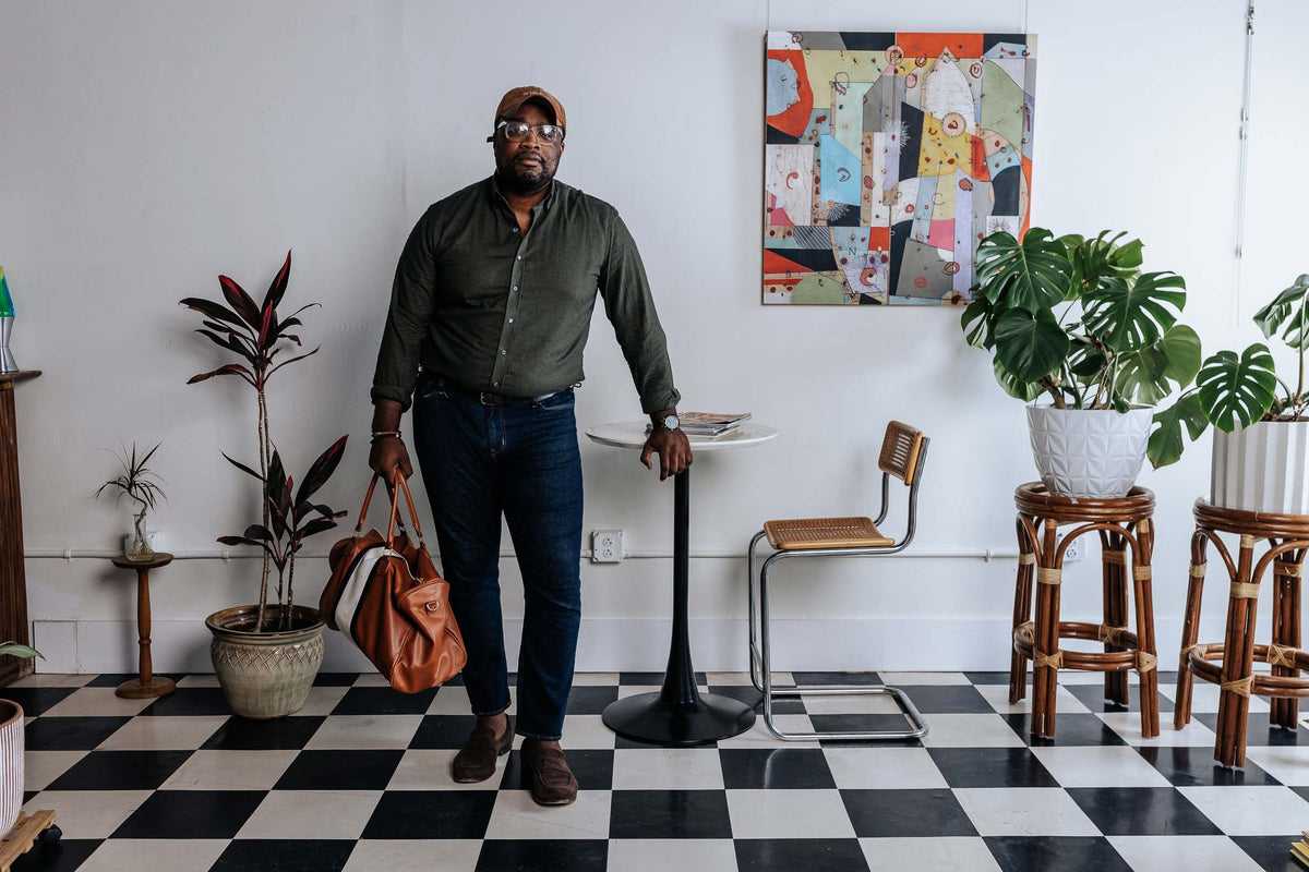 Man standing in a room with checkered floor, plants, and a colorful abstract painting on the wall.