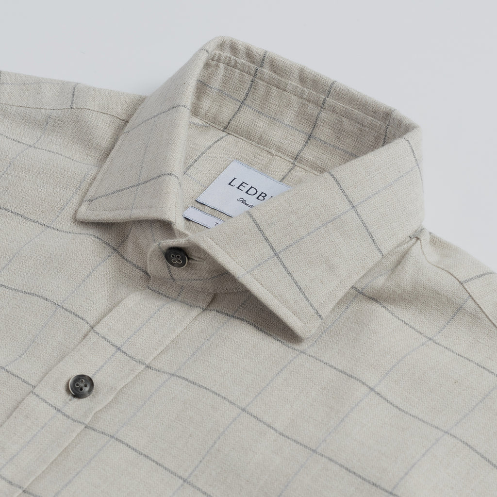 Closeup of the collar of a men's cream colored button down flannel with a large scale grey check 