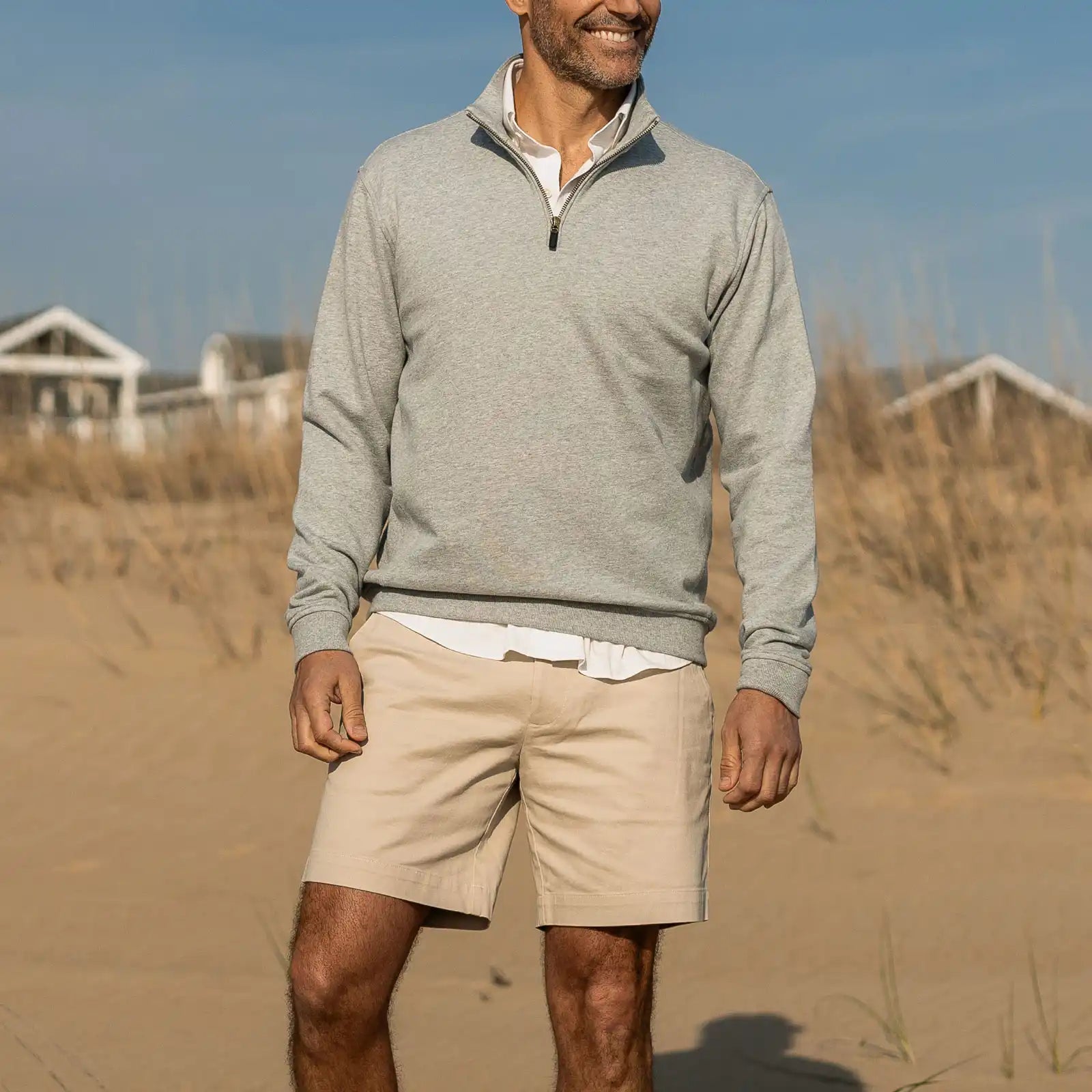 Man wearing a gray Ledbury cotton quarter zip pullover and beige shorts standing on a sandy beach.