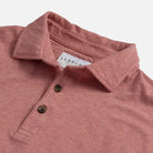 Close-up of a heathered light red polo shirt with a white Ledbury neck label and two dark buttons, photographed on a light gray background.