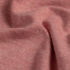 A close-up of draped heathered light red fabric showing its soft texture and fine knit detail.