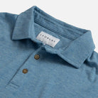 Close-up of a heathered blue polo shirt collar with two brown buttons and a visible LEDBURY neck label on a light gray background.