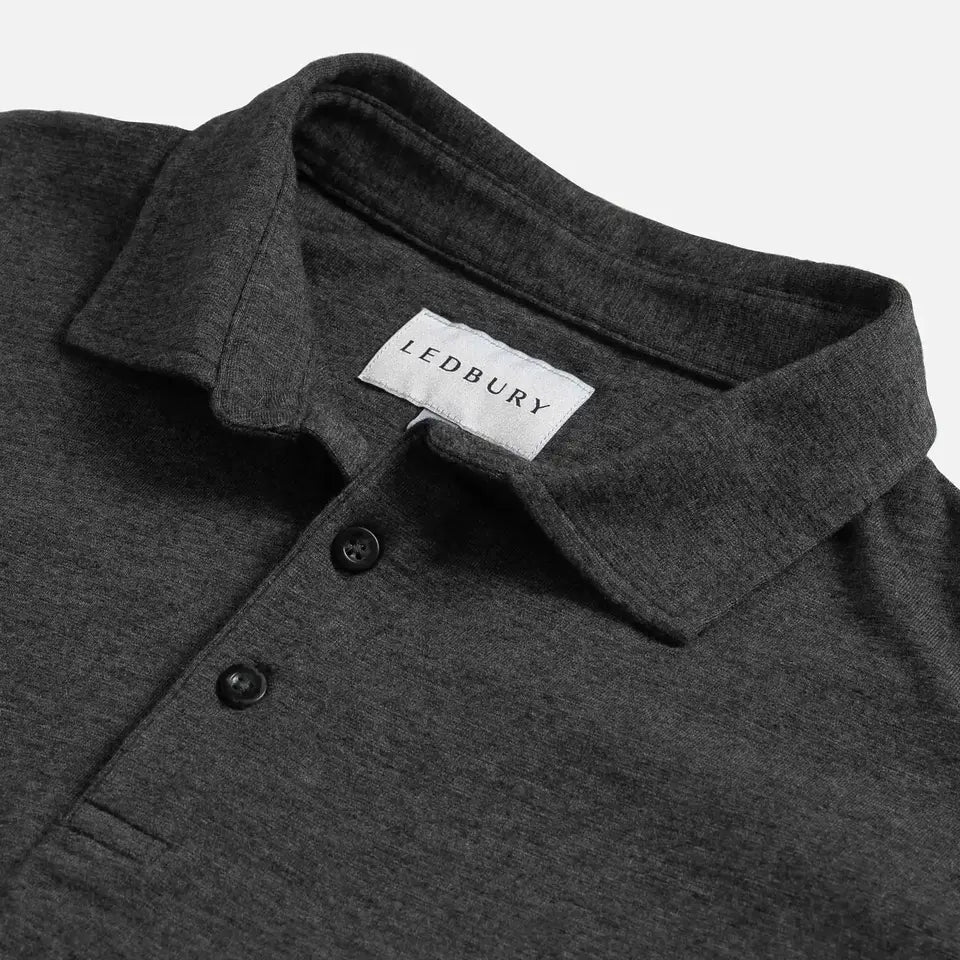 Close-up of a dark heather gray polo shirt collar with a white LEDBURY neck label and two dark buttons, photographed on a light gray background.