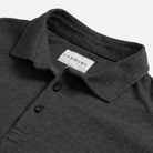Close-up of a dark heather gray polo shirt collar with a white LEDBURY neck label and two dark buttons, photographed on a light gray background.