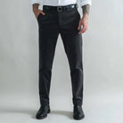 A man wearing slim-fit dark grey corduroy trousers, a black belt, a white shirt, and black leather boots, standing against a light gray studio background.