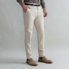 A man wearing slim-fit khaki trousers, styled with a black belt, a gray shirt, and tan suede Chelsea boots, shown from the waist down against a light gray studio background.