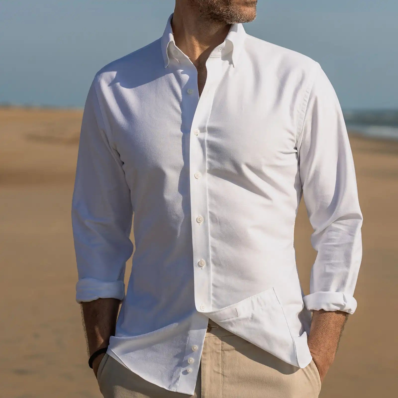 Man wearing a the white Mayfield Oxford button-up shirt with rolled-up sleeves on a beach.